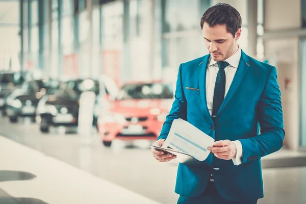 Jovem concessionário de automóveis em pé no showroom . — Fotografia de Stock