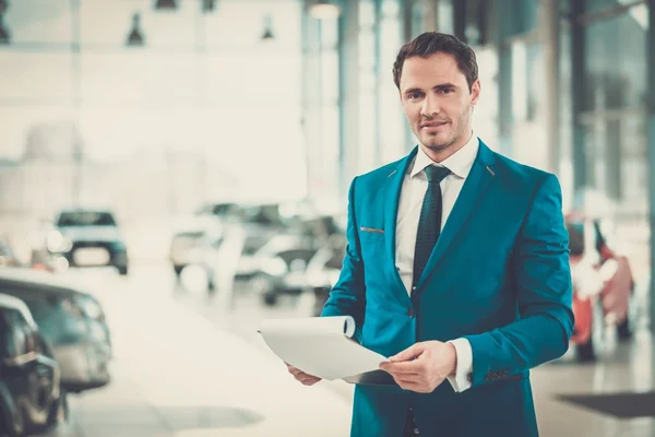 Young car dealer standing in showroom. — Stock Photo, Image