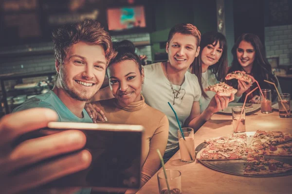 Wielorasowe znajomi, zabawa jedzenie pizzy w pizzerii. — Zdjęcie stockowe