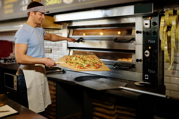 Pizzaiolo haciendo pizza en la cocina en la pizzería . — Foto de Stock
