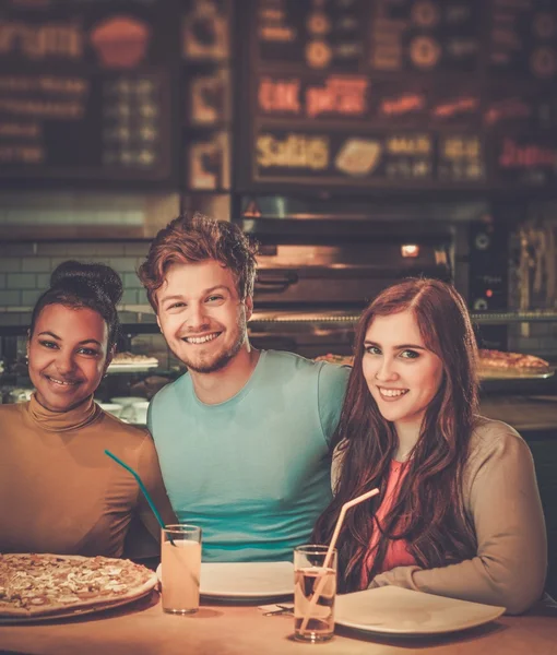 Multiraciale vrienden plezier pizza eten in pizzeria. — Stockfoto