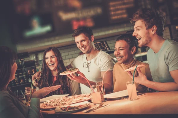 Amici multirazziali si divertono a mangiare pizza in pizzeria . — Foto Stock