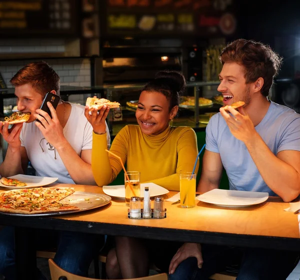 Multiraciale vrienden plezier pizza eten in pizzeria. — Stockfoto