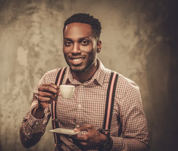 Стильный молодой черный мужчина с чашкой кофе позирует на темном фоне . — стоковое фото
