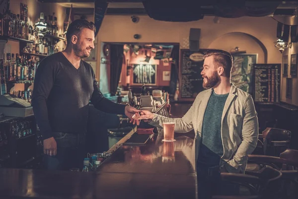 Stijlvolle man betalen voor bier door contante euro aan barman in pub. — Stockfoto