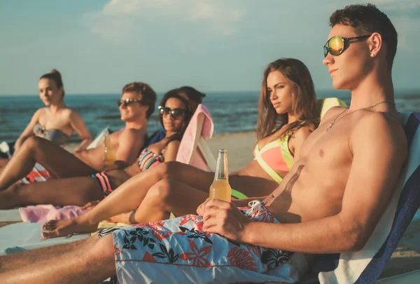 Grupp multi etniska vänner sola på en solstolar på stranden — Stockfoto