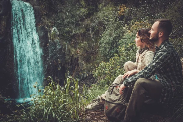 Beautiful woman hiker sitting near waterfall in deep forest. — Stock Photo, Image