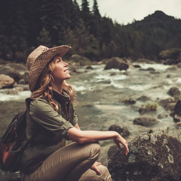 Belle femme randonneuse assise sur la pierre près de la rivière sauvage de montagne . — Photo