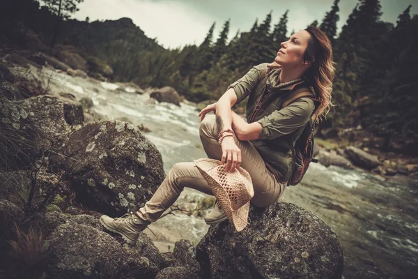 Bella donna escursionista seduto sulla pietra vicino fiume selvaggio montagna . — Foto Stock