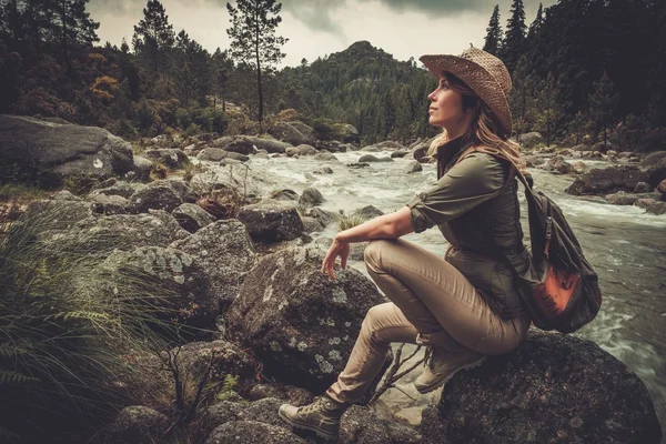 Mooie vrouw wandelaar zittend op de steen in de buurt van wilde berg rivier. — Stockfoto