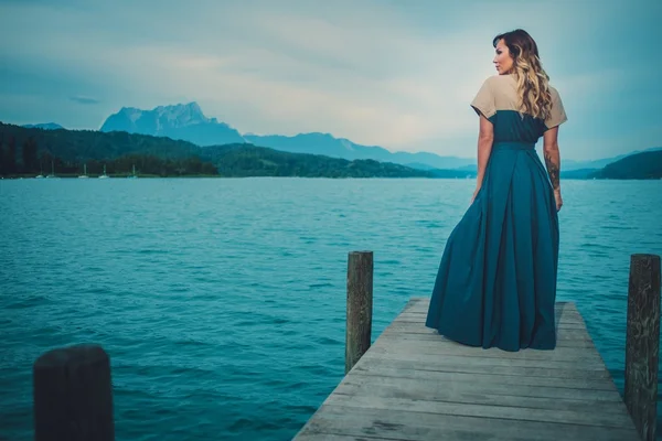 Goed geklede vrouw zittend op de houten pier met uitzicht op de rivier berg. — Stockfoto