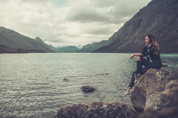 Gyönyörű nő pózol egy vad tó partján hegyek a háttérben. — Stock Fotó