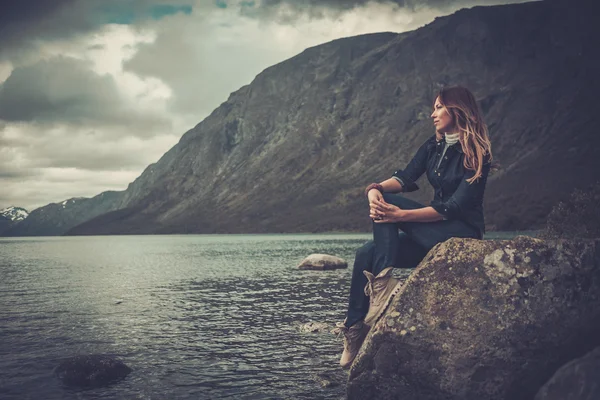 Mulher bonita posando na margem de um lago selvagem, com montanhas no fundo . — Fotografia de Stock