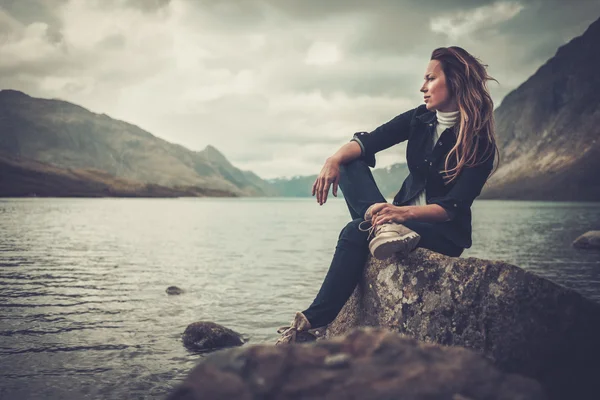 Bella donna in posa sulla riva di un lago selvaggio, con montagne sullo sfondo . — Foto Stock