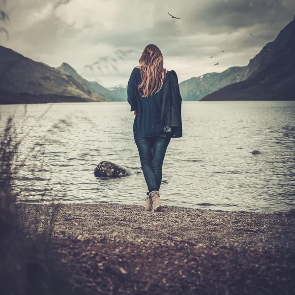 Mulher bonita posando na margem de um lago selvagem, com montanhas no fundo . — Fotografia de Stock