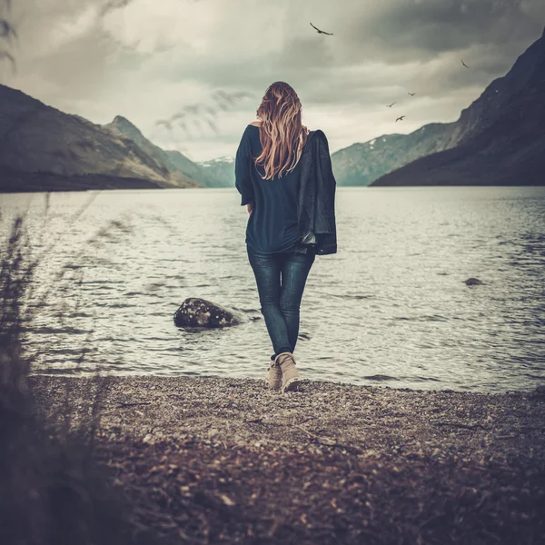 Bella donna in posa sulla riva di un lago selvaggio, con montagne sullo sfondo . — Foto Stock