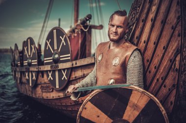 Viking warrior with sword and shield standing near Drakkar clipart