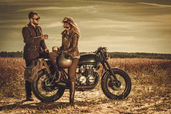 Elegante coppia di cafe racer sulle moto vintage personalizzate in un campo . — Foto Stock