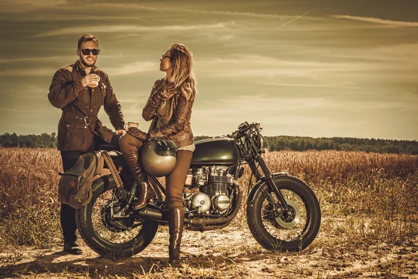 Stylish cafe racer couple on the vintage custom motorcycles in a field. — Stock Photo, Image