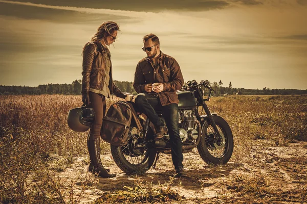 Stylish cafe racer couple on the vintage custom motorcycles in a field. — Stock Photo, Image