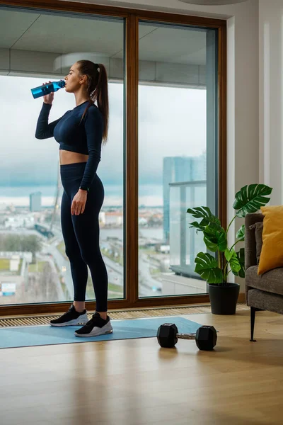 Slanke brunette vrouw drinkt water door panoramisch venster — Stockfoto