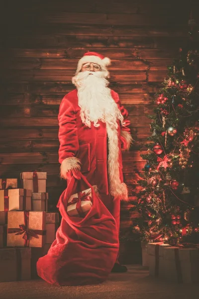 Παρουσιάζει τον Άγιο Βασίλη στο ξύλινο σπίτι εσωτερικό με το τσουβάλι γεμάτο των Χριστουγέννων — Φωτογραφία Αρχείου