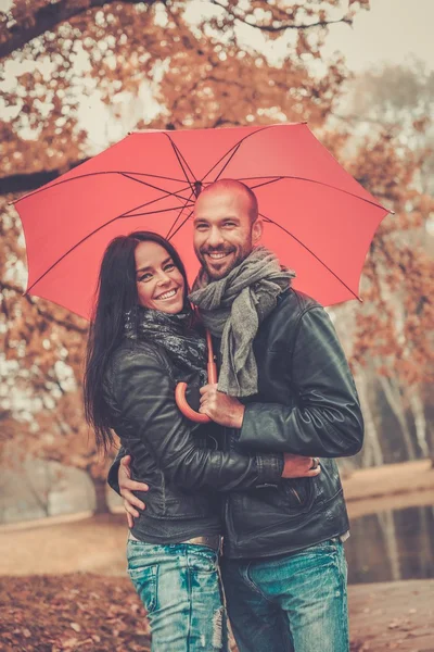 Счастливая пара средних лет с зонтиком на открытом воздухе в прекрасный дождливый осенний день — стоковое фото