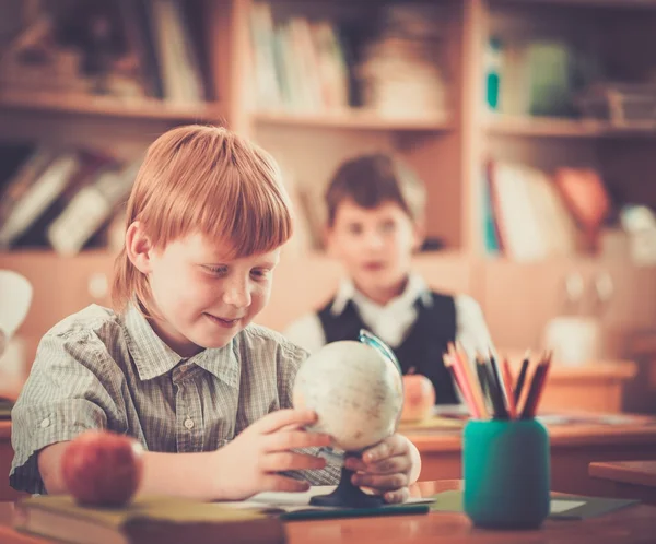 Petit écolier rousse derrière le bureau de l'école pendant les cours — Photo