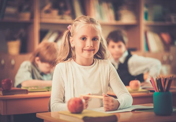 Pequeña colegiala sentada detrás del escritorio escolar durante la lección en la escuela —  Fotos de Stock