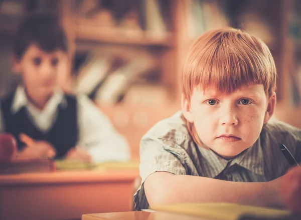 Pequeno estudante ruivo atrás da mesa da escola durante a aula — Fotografia de Stock