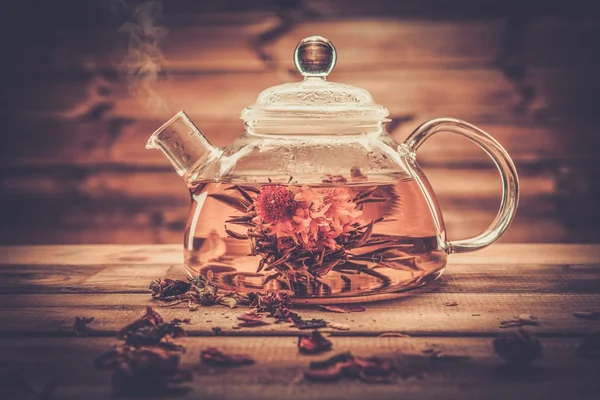 Bule de vidro com flor de chá florescendo dentro contra fundo de madeira — Fotografia de Stock