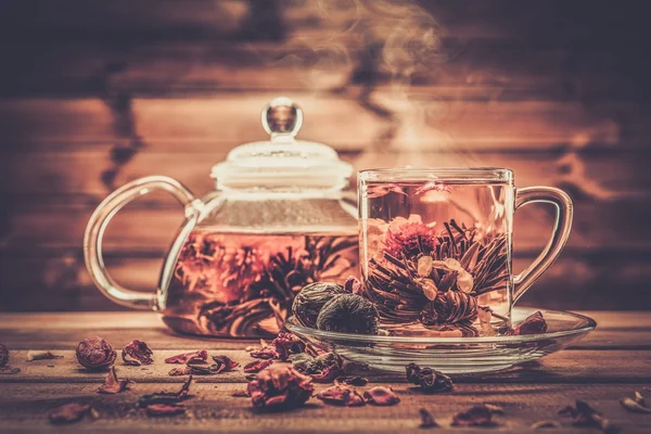 Bule e xícara de vidro com flor de chá florescendo dentro contra fundo de madeira — Fotografia de Stock