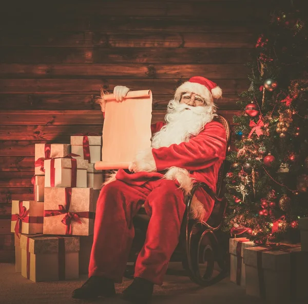 Santa Claus in wooden home interior holding blank wish list scroll — Stockfoto