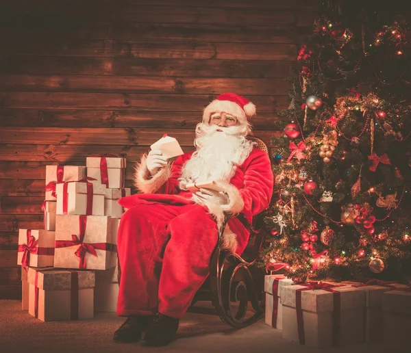 Père Noël assis sur chaise à bascule dans l'intérieur de la maison en bois avec des lettres dans les mains — Photo