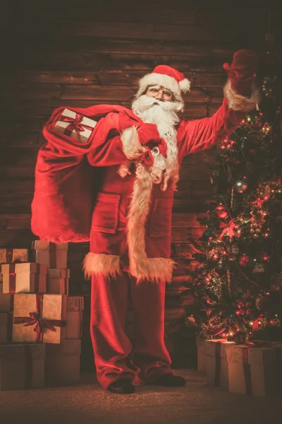 Père Noël à l'intérieur de la maison en bois avec sac plein de cadeaux de Noël — Photo