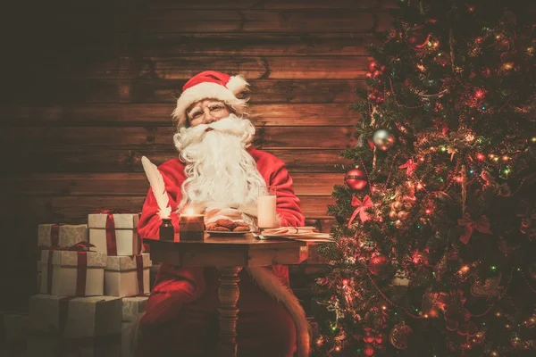 Santa claus in houten huis interieur vergadering achter tafel met melk en havermout cookies — Stockfoto