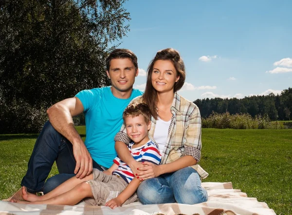 Young family with their child sitting on a blanket outdoors — Stock Photo, Image