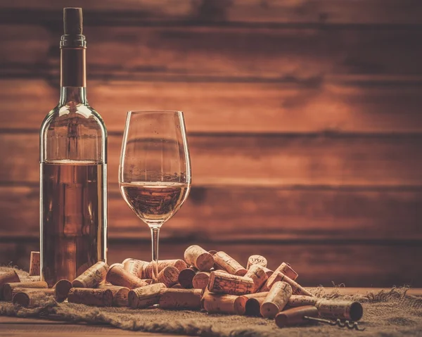 Butelkę i kieliszek białego wina, na drewnianym stole wśród korki — Zdjęcie stockowe