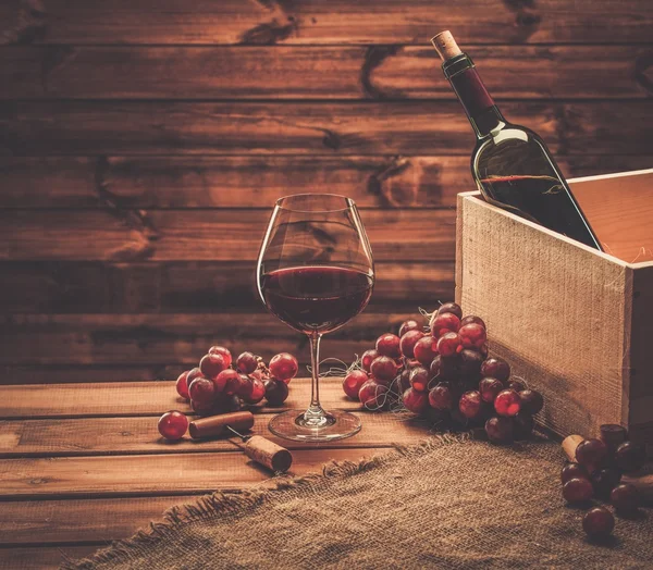Бутылка, стекло и красный виноград на деревянном столе — стоковое фото