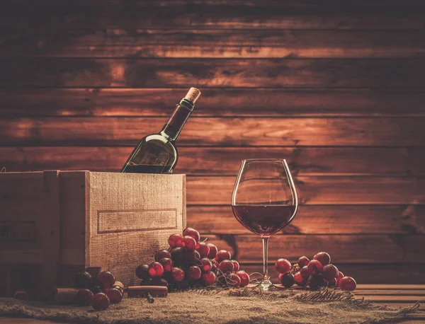 Garrafa, vidro e uva vermelha em uma mesa de madeira — Fotografia de Stock