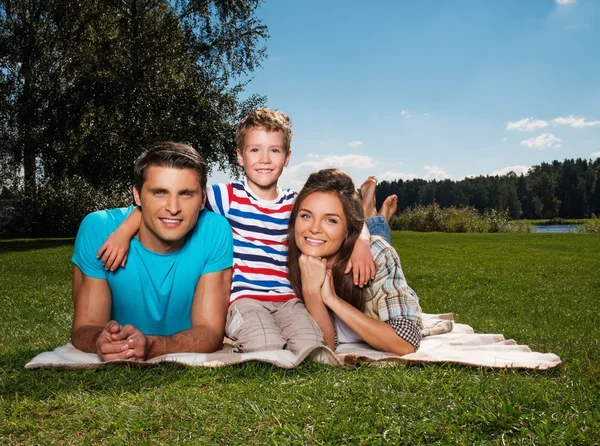 Ung familj med barnet liggande på en filt utomhus — Stockfoto