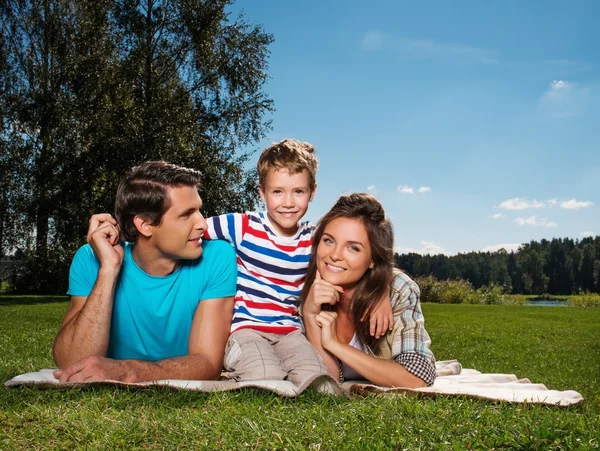 Familia joven con su hijo acostado en una manta al aire libre —  Fotos de Stock