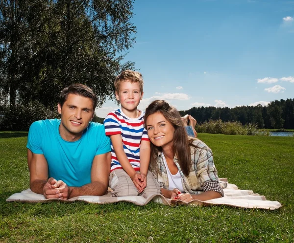 Jonge gezin met hun kind liggend op een deken in de buitenlucht — Stockfoto