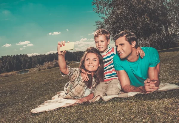 Família jovem com seu filho fazendo selfie em um cobertor ao ar livre — Fotografia de Stock