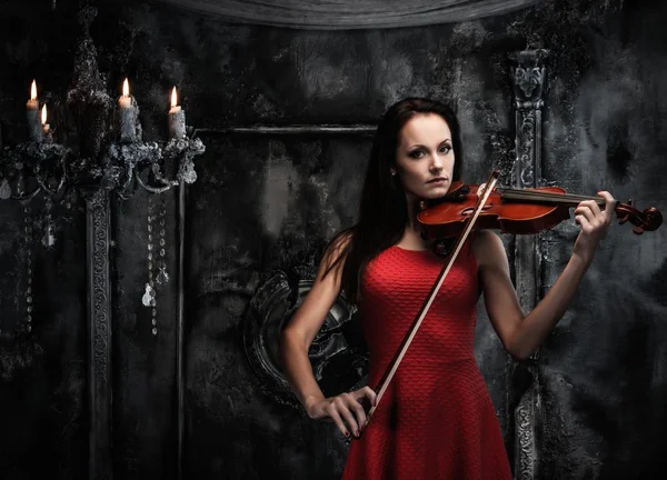 Jovem de vestido vermelho tocando violino no interior místico — Fotografia de Stock