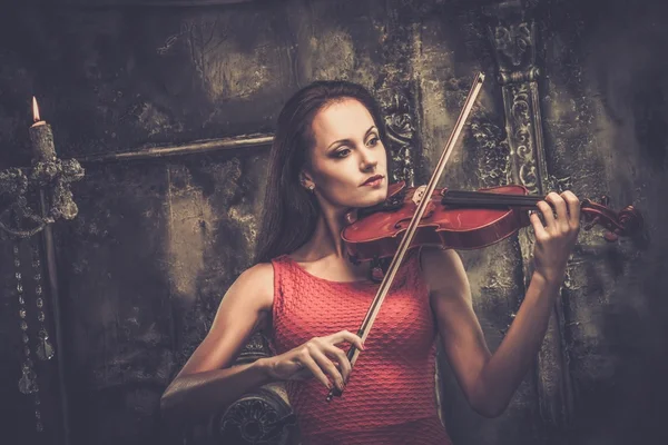 Молодая женщина в красном платье играет на скрипке в мистическом интерьере — стоковое фото