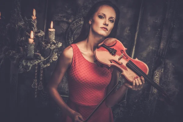Mladá žena v červených šatech, které hrají housle v mystic interiéru — Stock fotografie