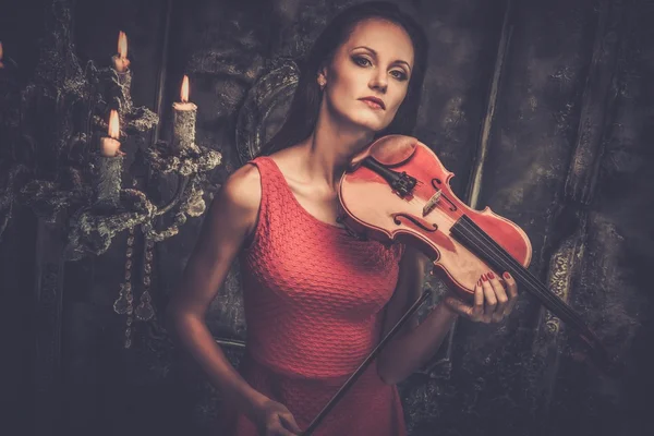 Jovem de vestido vermelho tocando violino no interior místico — Fotografia de Stock