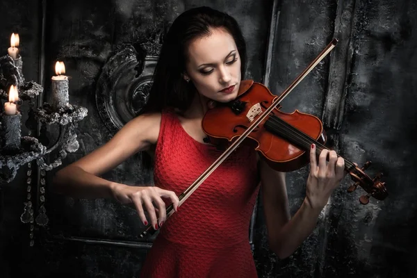 Jovem de vestido vermelho tocando violino no interior místico — Fotografia de Stock