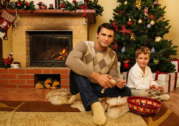 Padre joven con su hijo cerca de la chimenea en el interior de la casa decorada de Navidad —  Fotos de Stock